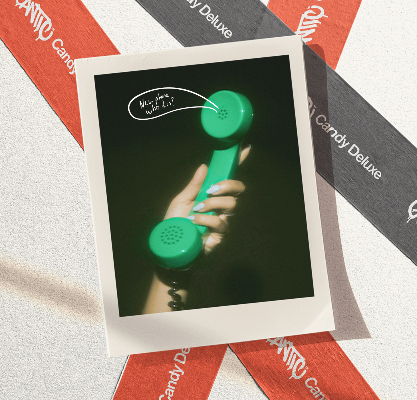 Polaroid-style photo — hand holding a green handset; handwritten 'New phone who dis?' and background ribbons reading 'Candy Deluxe'.